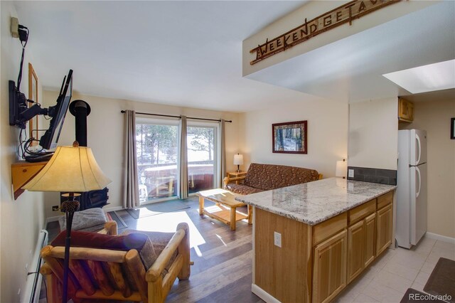 kitchen featuring baseboards, light stone counters, open floor plan, freestanding refrigerator, and a peninsula