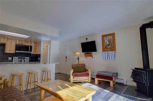 living area featuring dark wood-style floors, a wood stove, a baseboard heating unit, and baseboards