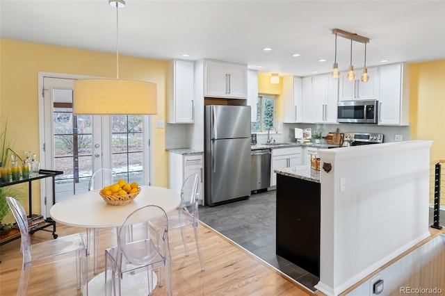 kitchen featuring pendant lighting, white cabinets, stainless steel appliances, and light hardwood / wood-style floors