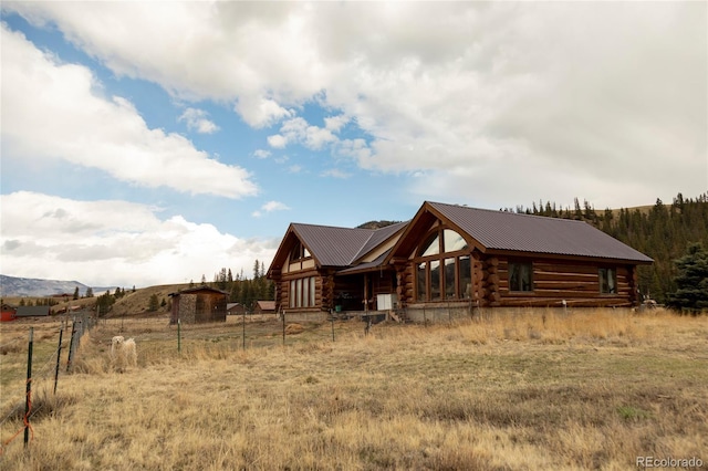 rear view of house featuring log exterior, fence, and metal roof