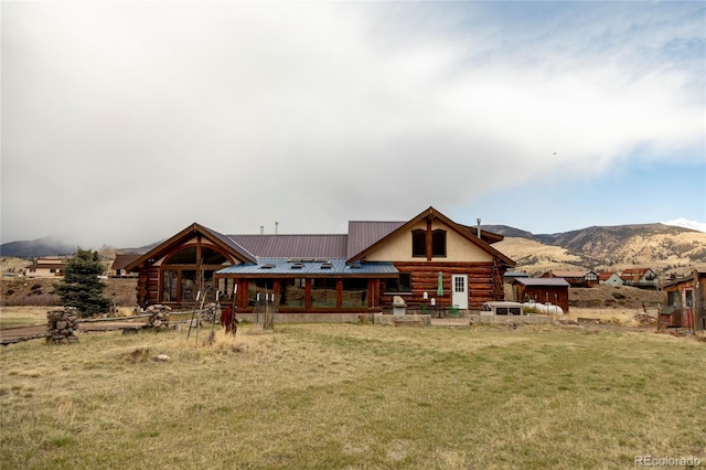 rear view of house with log siding, a yard, a mountain view, and metal roof
