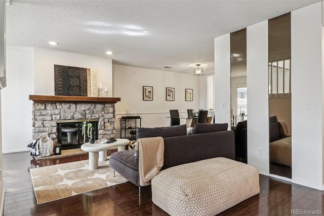 living room featuring dark hardwood / wood-style floors, a stone fireplace, and a textured ceiling