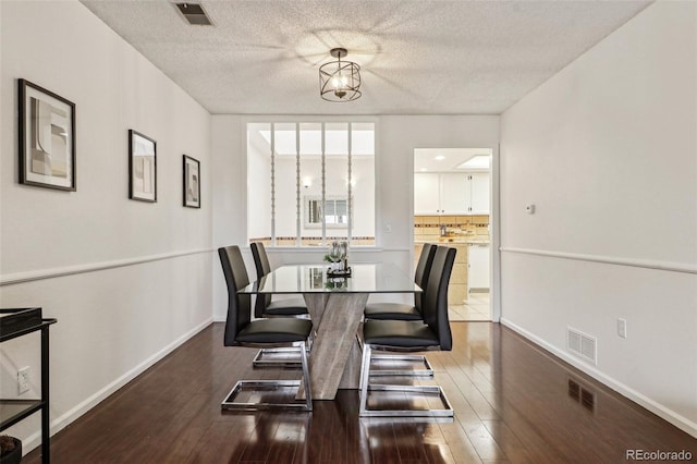 dining area with dark wood-type flooring, a notable chandelier, and a textured ceiling