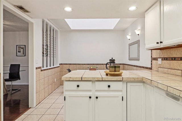 kitchen featuring tile walls, a skylight, white cabinets, light tile patterned flooring, and kitchen peninsula