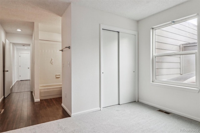 unfurnished bedroom featuring multiple windows, dark carpet, a textured ceiling, and a closet