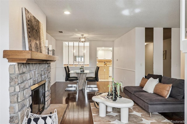 living room with a stone fireplace, dark wood-style floors, visible vents, and a textured ceiling