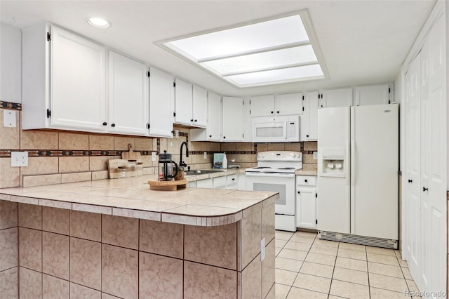 kitchen with light tile patterned floors, decorative backsplash, a peninsula, white cabinets, and white appliances
