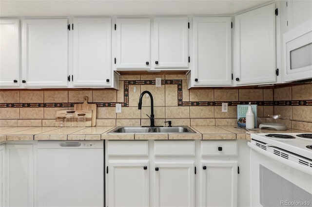 kitchen featuring light countertops, decorative backsplash, white cabinets, white appliances, and a sink