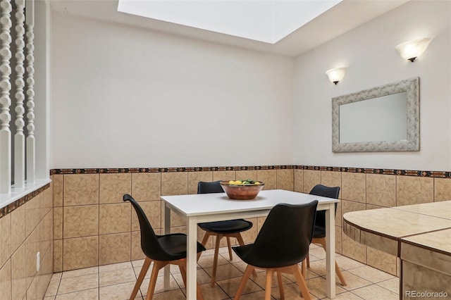 dining room featuring light tile patterned floors, a wainscoted wall, a skylight, and tile walls