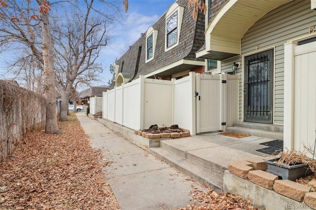 view of side of property featuring a gate, mansard roof, fence, and a shingled roof