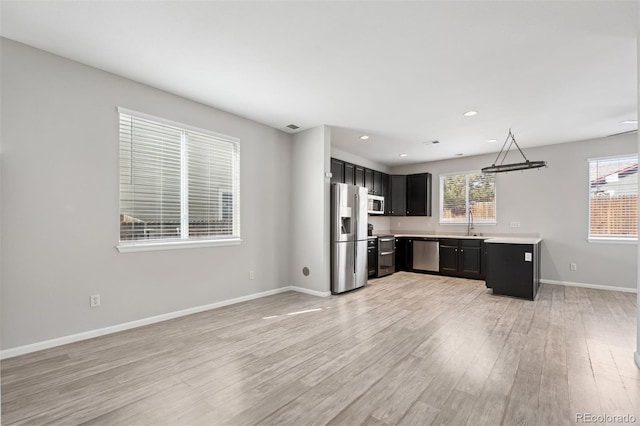 kitchen with plenty of natural light, light wood-style flooring, appliances with stainless steel finishes, light countertops, and dark cabinetry