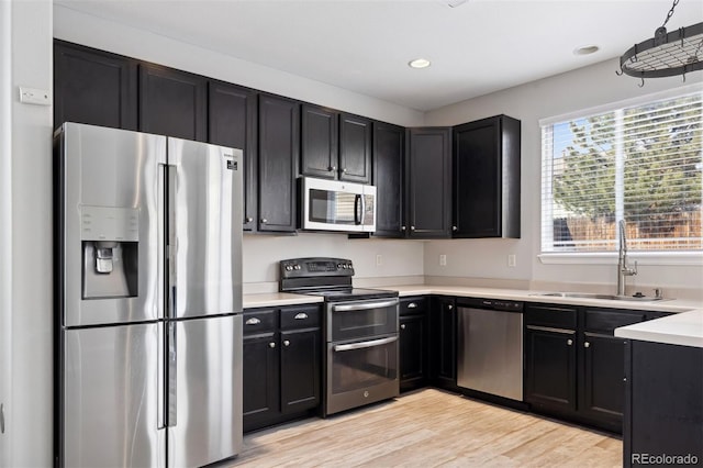 kitchen featuring light countertops, appliances with stainless steel finishes, a sink, light wood-type flooring, and dark cabinetry