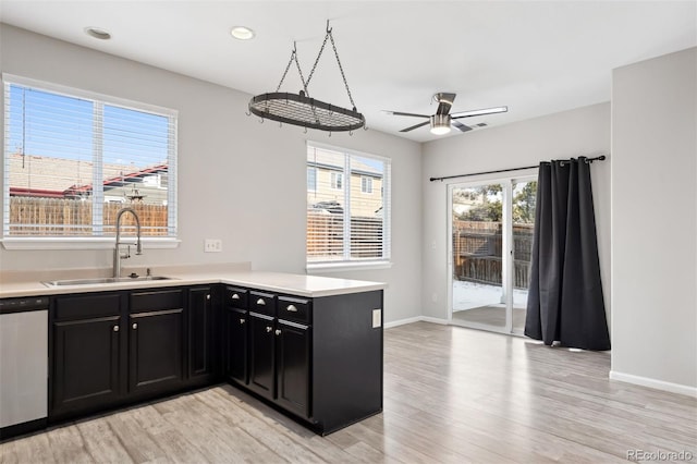 kitchen with light wood-style flooring, a sink, light countertops, stainless steel dishwasher, and dark cabinetry