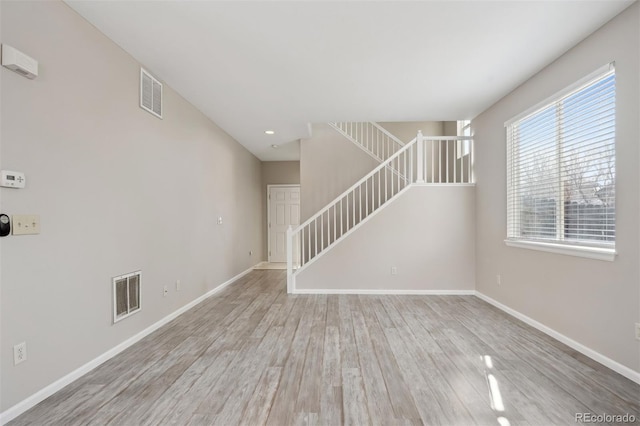 unfurnished living room featuring light wood finished floors, baseboards, stairs, and visible vents