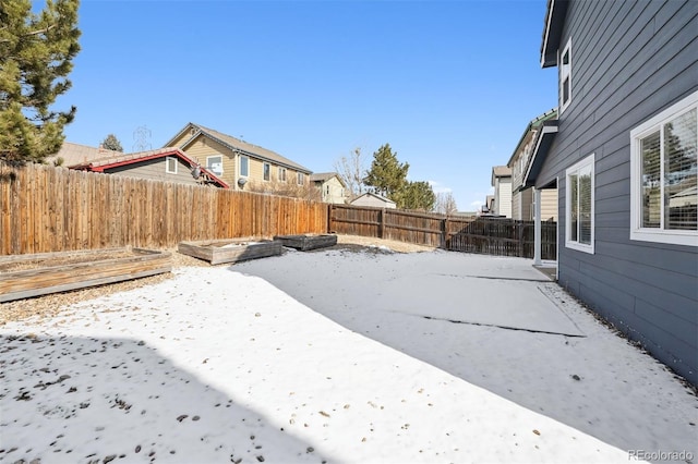 yard layered in snow with a patio, a fenced backyard, and a vegetable garden