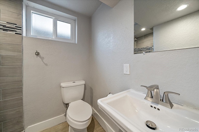 6026 Iris Way, Arvada, CO 80004 - bathroom featuring toilet, baseboards, a sink, wood finished floors, and a textured wall