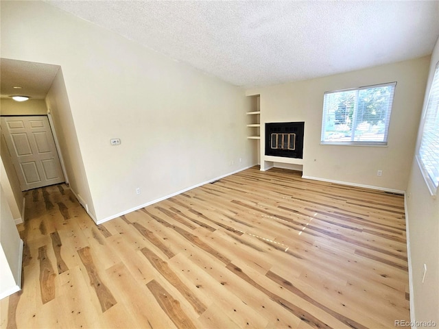 unfurnished living room featuring light wood-type flooring, a textured ceiling, and built in shelves