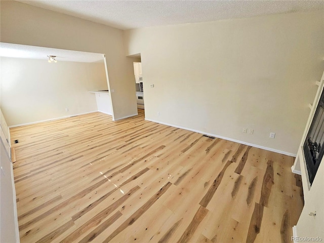 empty room with light wood-type flooring and a textured ceiling