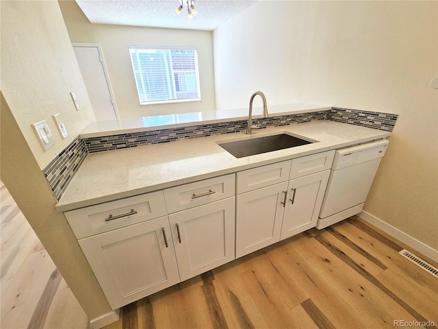 kitchen featuring a textured ceiling, light stone countertops, white dishwasher, light hardwood / wood-style floors, and sink