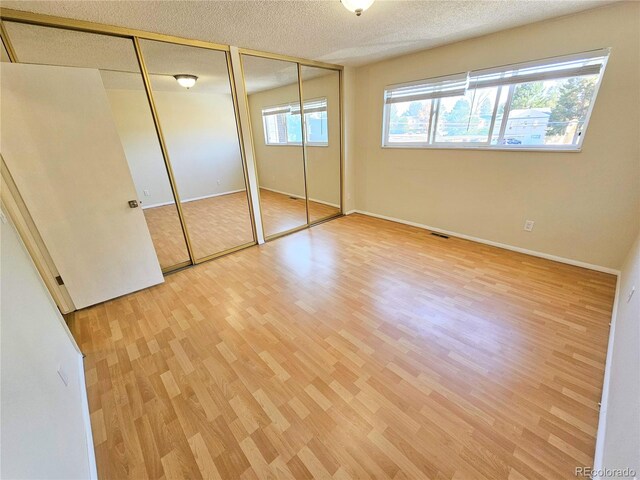 unfurnished bedroom with a textured ceiling, light hardwood / wood-style flooring, and two closets