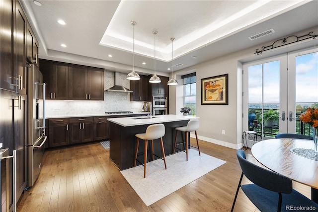 kitchen featuring dark brown cabinets, a kitchen breakfast bar, plenty of natural light, wall chimney exhaust hood, and visible vents