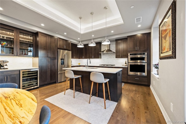kitchen with wine cooler, wall chimney range hood, a kitchen bar, a sink, and appliances with stainless steel finishes