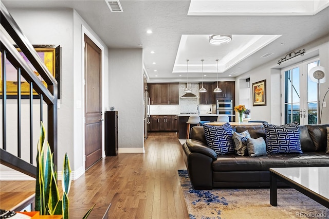 living room featuring visible vents, baseboards, light wood-style floors, a tray ceiling, and recessed lighting