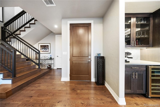 foyer featuring beverage cooler, visible vents, wood finished floors, and stairway