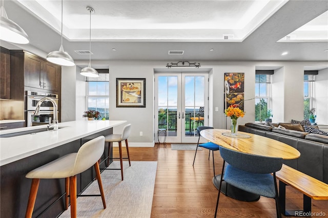 interior space featuring a raised ceiling, french doors, light wood finished floors, and visible vents