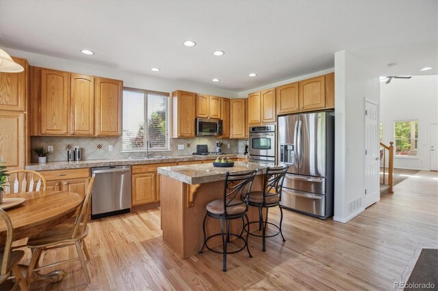 10448 Kicking Horse Dr, Littleton, CO 80125 - kitchen featuring stainless steel appliances, light wood-style flooring, a kitchen island, a breakfast bar, and recessed lighting