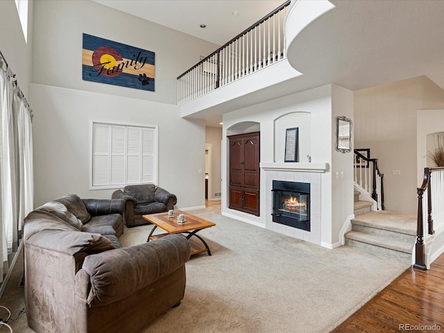 carpeted living area with a fireplace, a towering ceiling, stairway, wood finished floors, and baseboards