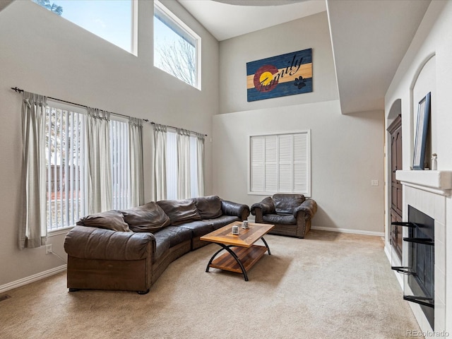 living room featuring light carpet, a glass covered fireplace, a towering ceiling, and baseboards