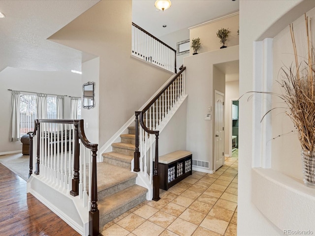 staircase featuring visible vents, baseboards, a high ceiling, and a textured ceiling