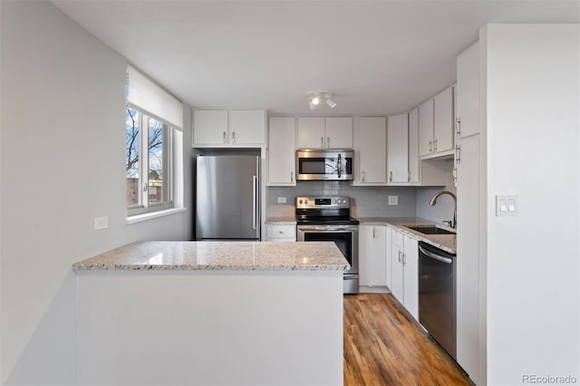 kitchen featuring decorative backsplash, kitchen peninsula, stainless steel appliances, sink, and white cabinets