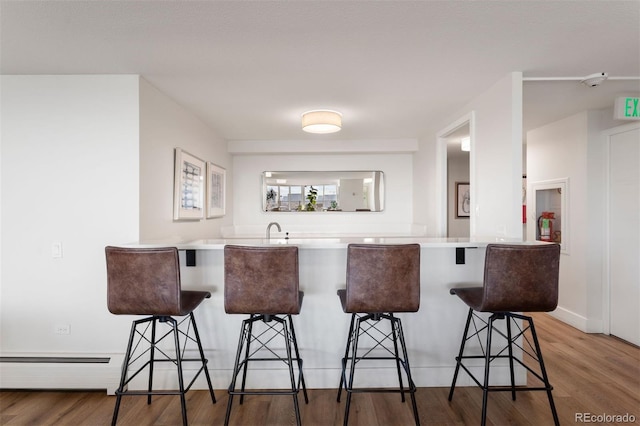 kitchen with a kitchen breakfast bar, light hardwood / wood-style floors, kitchen peninsula, and a baseboard heating unit