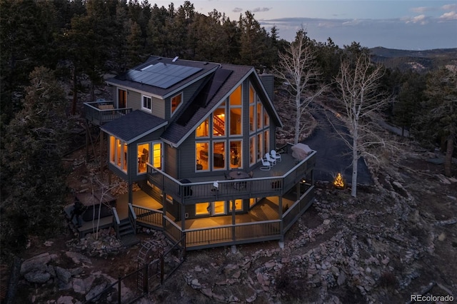13452 Riley Peak Rd, Conifer, CO 80433 - back of house with roof mounted solar panels, a balcony, a forest view, and a deck