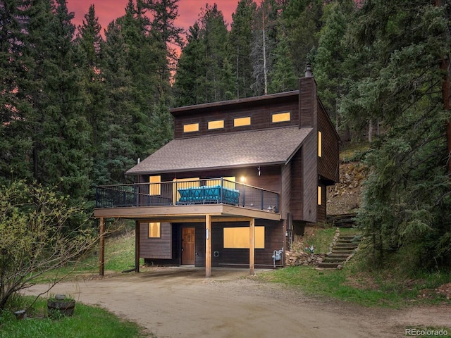 28272 Shadow Mountain Dr, Conifer, CO 80433 - view of front facade with dirt driveway, a chimney, stairway, a wooden deck, and a forest view