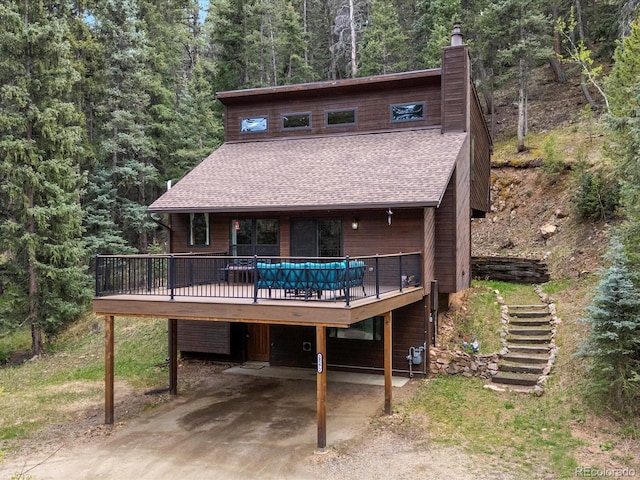 28272 Shadow Mountain Dr, Conifer, CO 80433 - view of front facade featuring a chimney, stairs, roof with shingles, a deck, and a forest view