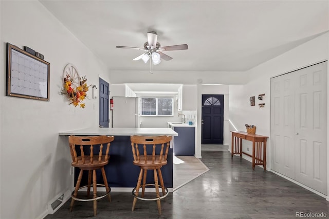 kitchen featuring freestanding refrigerator, a peninsula, light countertops, a kitchen bar, and a sink