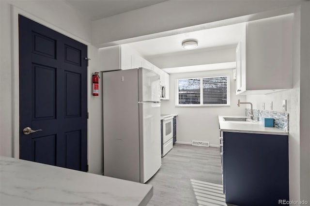 kitchen featuring light wood-style flooring, white appliances, a sink, visible vents, and white cabinets