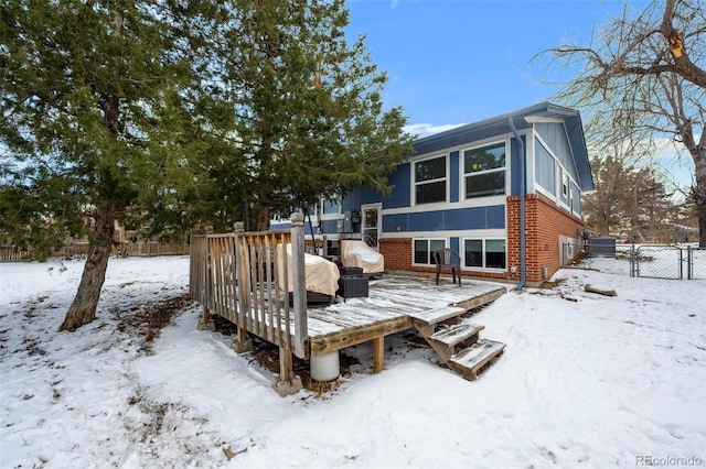 snow covered rear of property with a wooden deck, a gate, fence, and brick siding