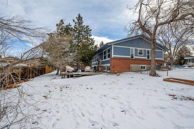 view of snowy exterior with a wooden deck, fence, and brick siding