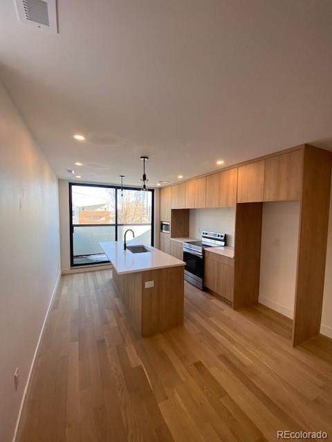 kitchen with sink, an island with sink, decorative light fixtures, stainless steel range with electric cooktop, and light wood-type flooring