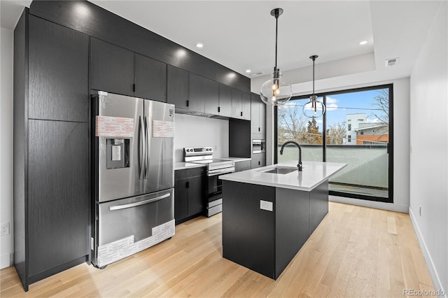 kitchen featuring dark cabinets, stainless steel appliances, a sink, light countertops, and decorative light fixtures