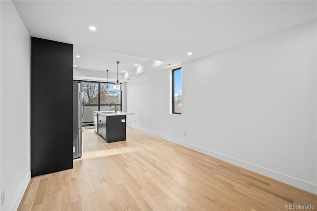 kitchen featuring a kitchen island with sink, a sink, light wood-style floors, open floor plan, and pendant lighting