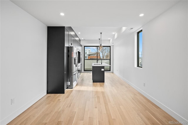 kitchen featuring pendant lighting, light wood finished floors, light countertops, a kitchen island, and stainless steel fridge with ice dispenser