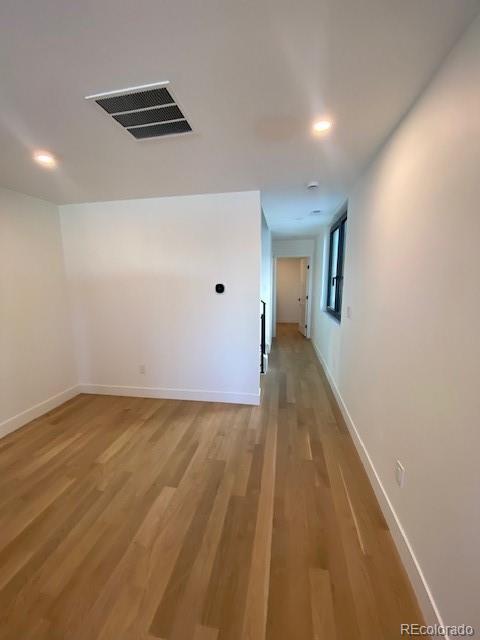 hall featuring light wood-style flooring, visible vents, baseboards, and recessed lighting