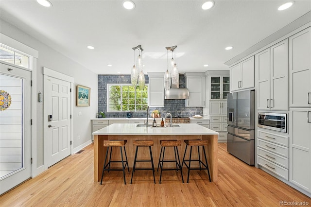 8256 E 28th Dr, Denver, CO 80238 - kitchen featuring stainless steel appliances, wall chimney range hood, light wood finished floors, a sink, and a breakfast bar area
