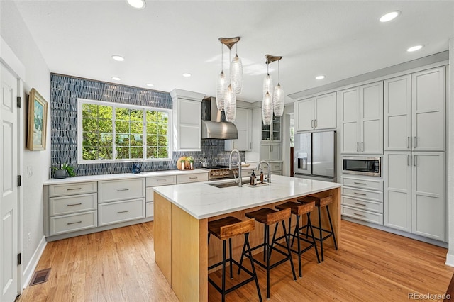 8256 E 28th Dr, Denver, CO 80238 - kitchen with stainless steel appliances, light wood-style floors, backsplash, wall chimney exhaust hood, and a kitchen bar