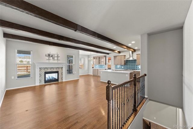 living room featuring beamed ceiling, light hardwood / wood-style floors, and a tile fireplace